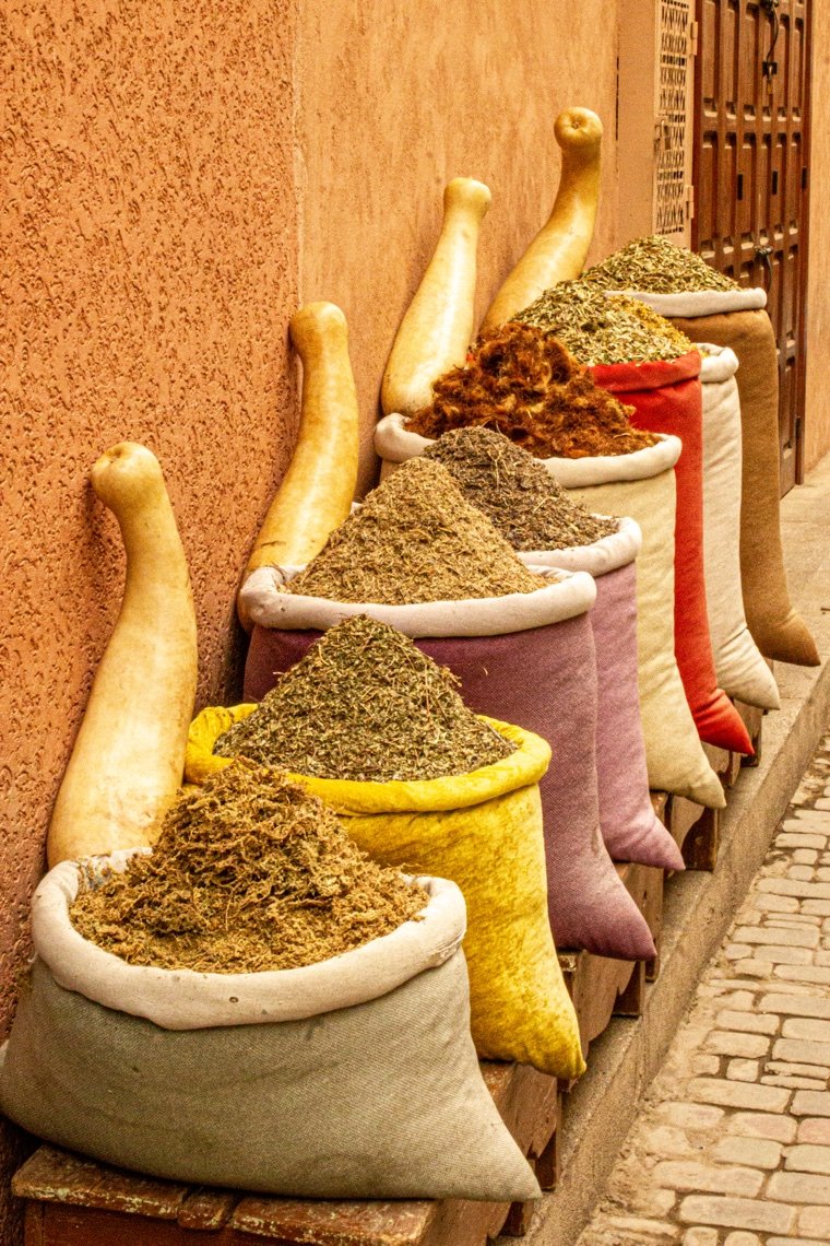 Sacos de especias apoyados contra una pared de color terracota, en la medina de Marrakech.