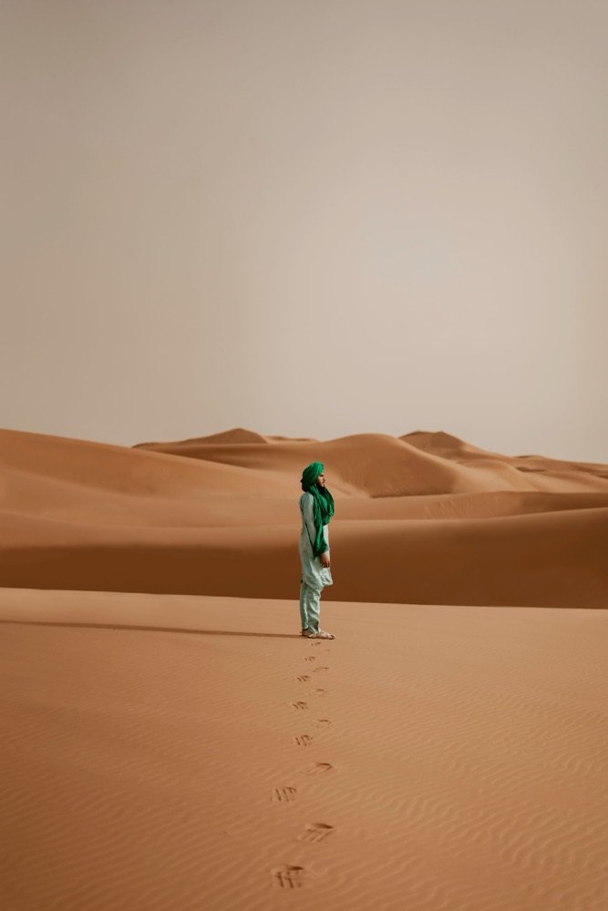 Una figura sola entre dunas de arena rojiza, con sus huellas detrás.