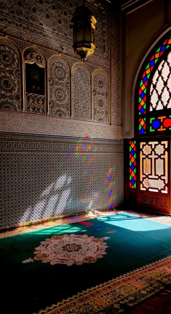 Interior de un palacio de Marrakech con la luz entrando por vidrieras de colores.